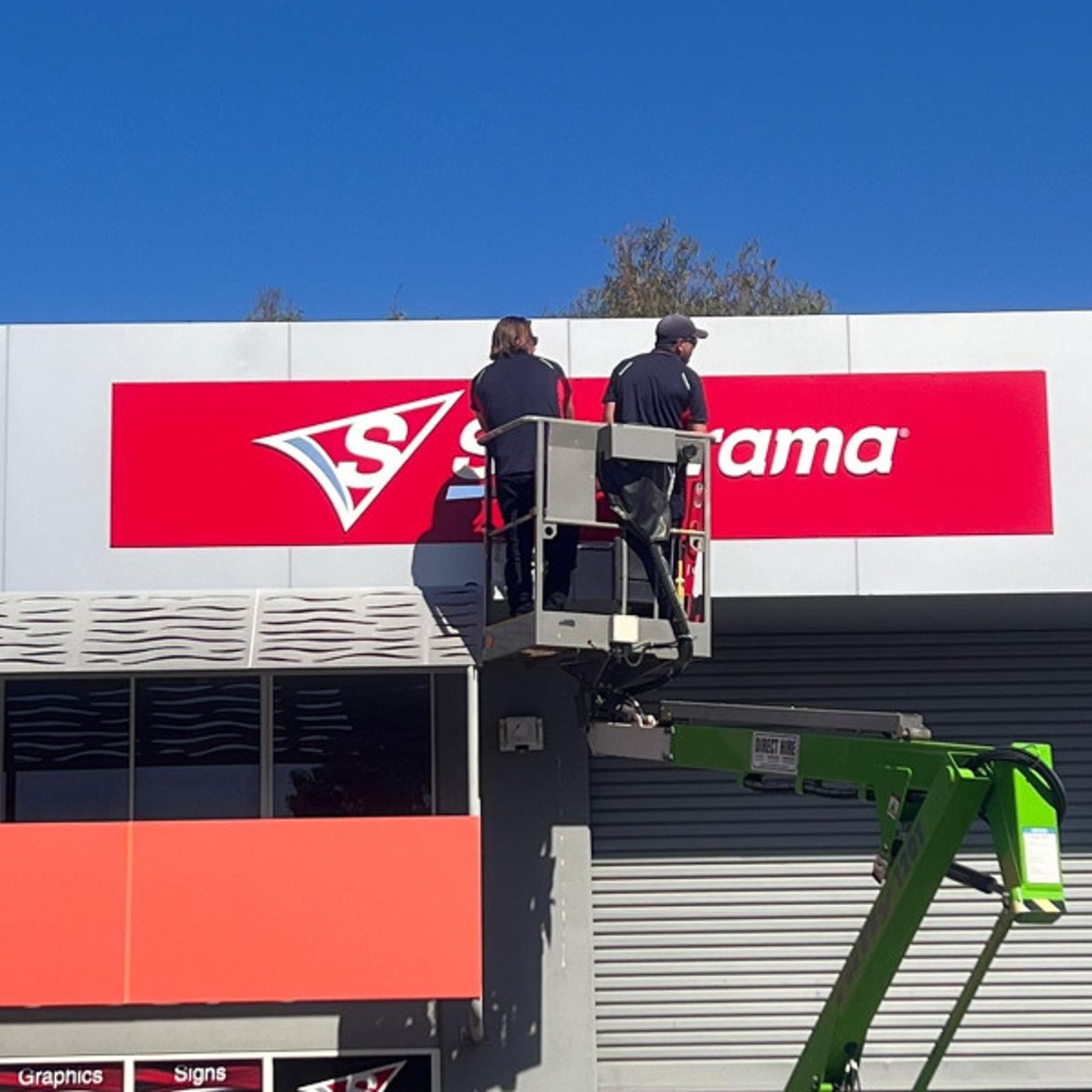 Two Signarama installers on a cherry picker installing a signarama sign at the top of the showroom