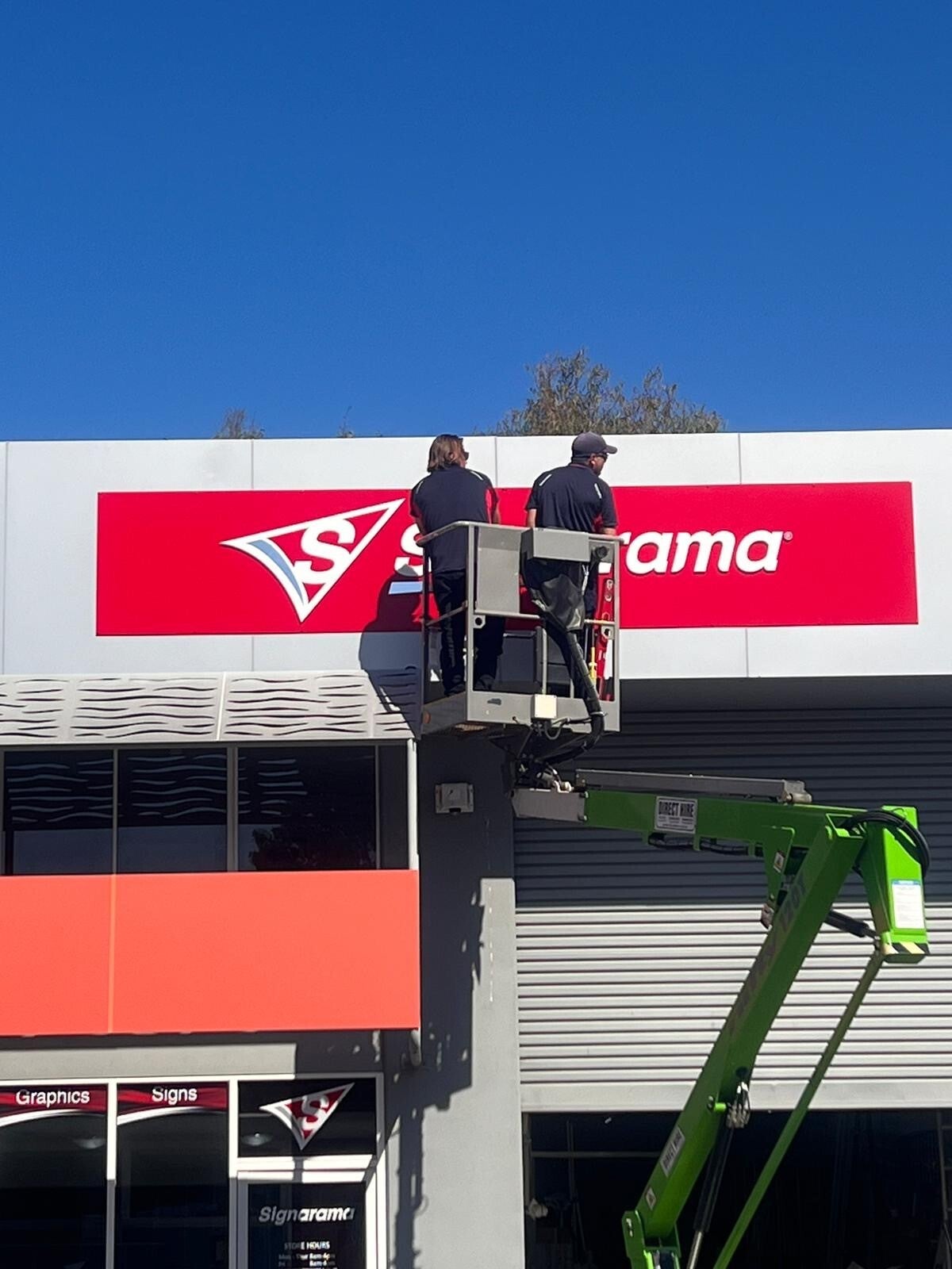 Two Signarama installers on a cherry picker installing a signarama sign at the top of the showroom
