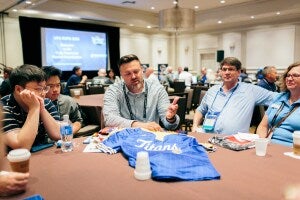A Fully Promoted employee sitting at a table with other vendors and franchisees at a trade show.