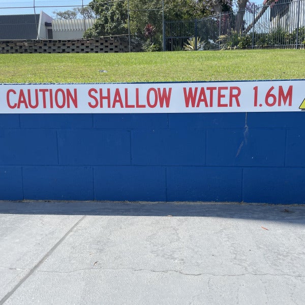 Caution sign indicating shallow water attached to pool wall by Signarama Brendale.
