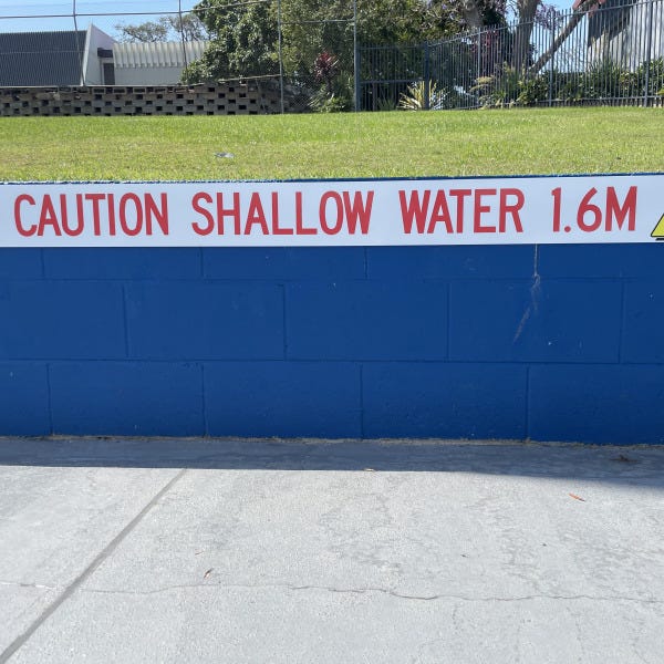 Caution sign indicating shallow water attached to pool wall by Signarama Brendale.