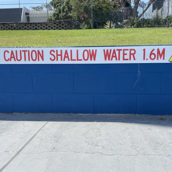 Caution sign indicating shallow water attached to pool wall by Signarama Brendale.