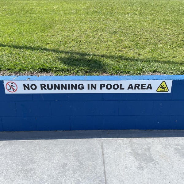 Caution sign with "No running in pool area" attached to blue wall by Signarama Brendale.