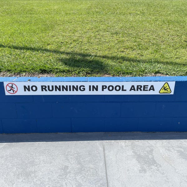 Caution sign with "No running in pool area" attached to blue wall by Signarama Brendale.