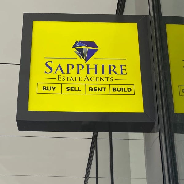 Illuminated lightbox signage featuring bright yellow and blue graphics for Sapphire Estate Agents attached adjacent to wall by Signarama Brisbane CBD..