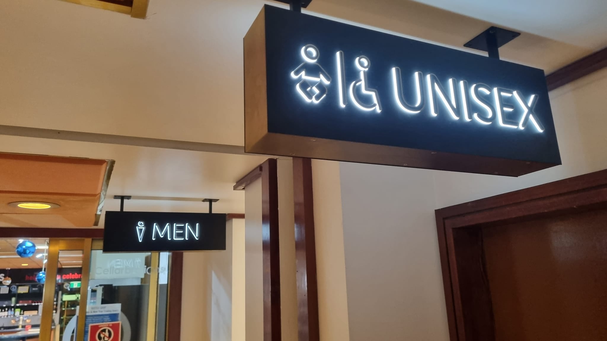 Professionally installed ADA-compliant signage featuring black overhead light-box signs with illuminated white "UNISEX" and "MEN" lettering and universal accessibility pictograms.