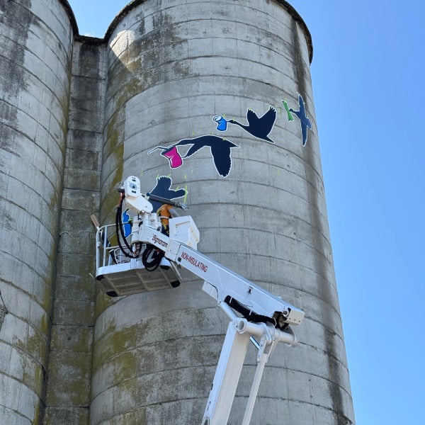 Colorful exterior graphics being applied to a tall concrete silo