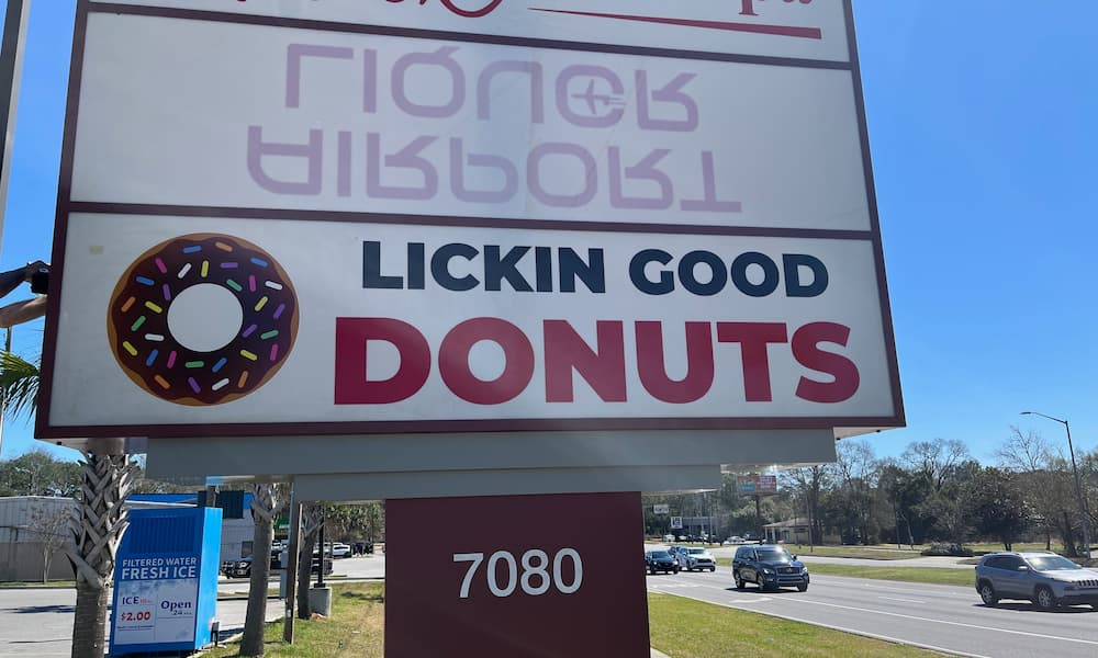 A large, rectangular roadside pylon sign for LICKIN GOOD DONUTS
