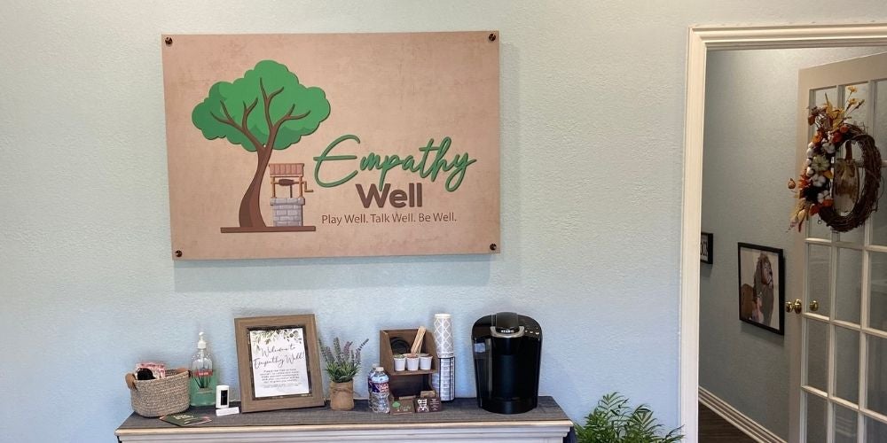 An indoor reception area with a wooden sign on a light blue wall that reads Empathy Well.