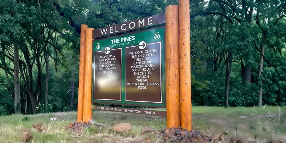 A large outdoor camp directory sign made of green panels and thick rustic wooden log posts.