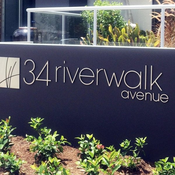 Branded Gold Metal Sign in outdoor garden on dark wall with logo | Signarama