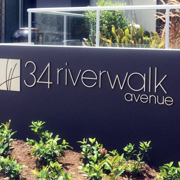 Branded Gold Metal Sign in outdoor garden on dark wall with logo | Signarama