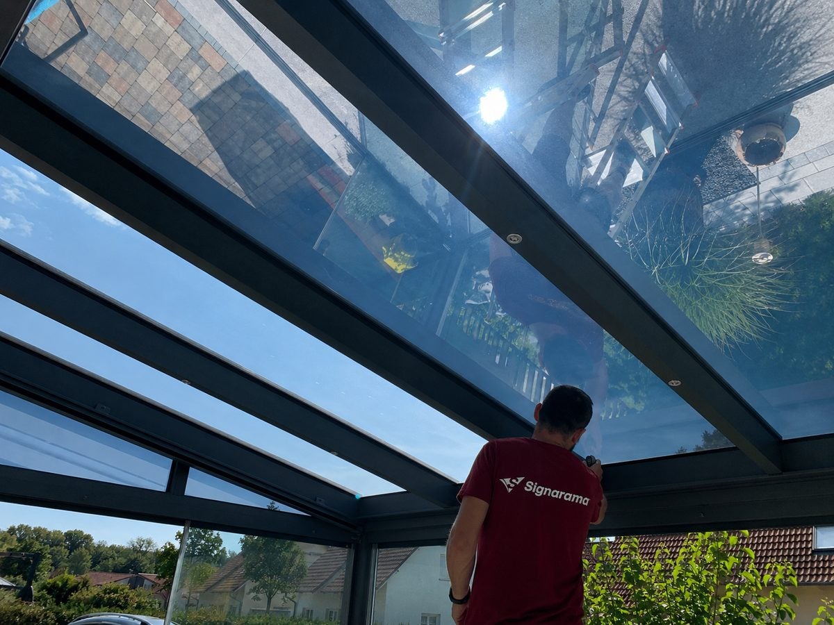 Signarama-Monteur bei der Montage einer Sonnenschutzfolie auf einem Terrassendach
