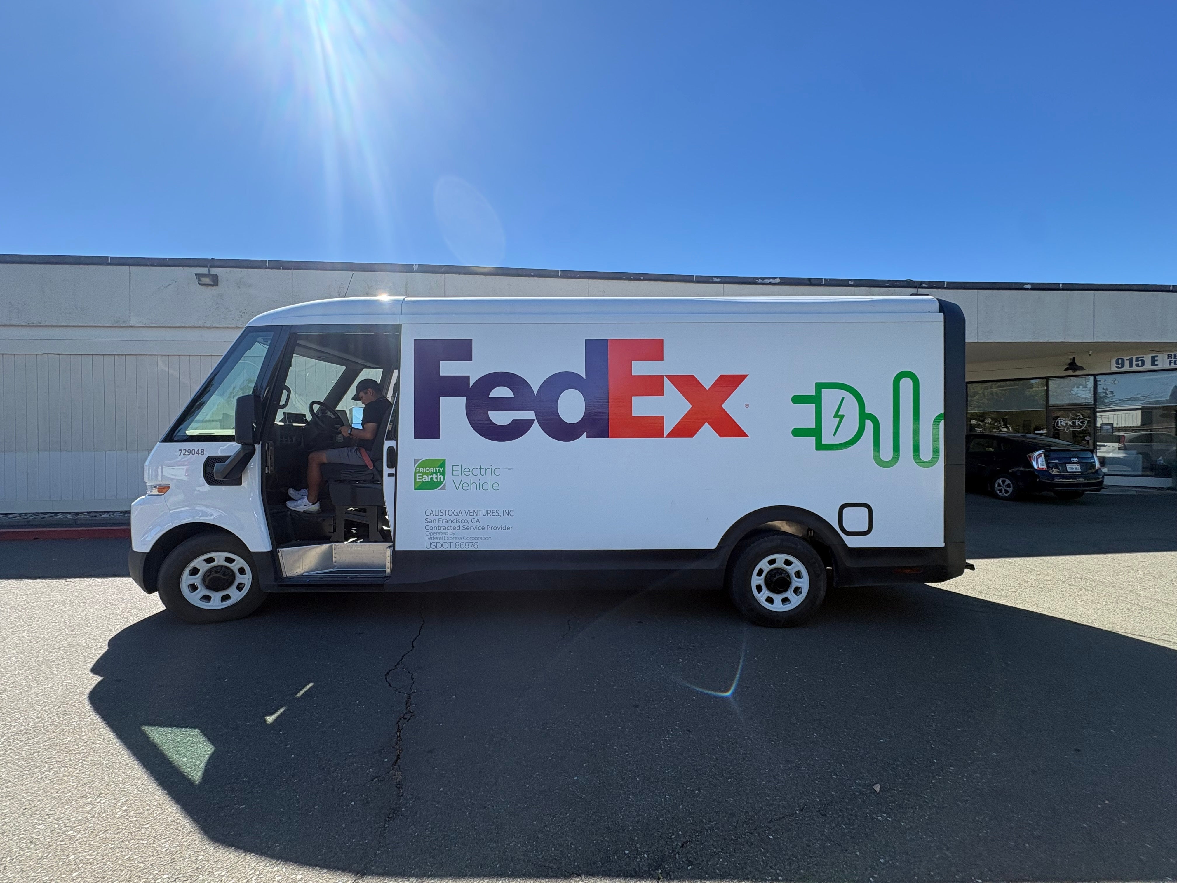 Driver-side view of a FedEx BrightDrop electric delivery van with FedEx and Priority Earth graphics.