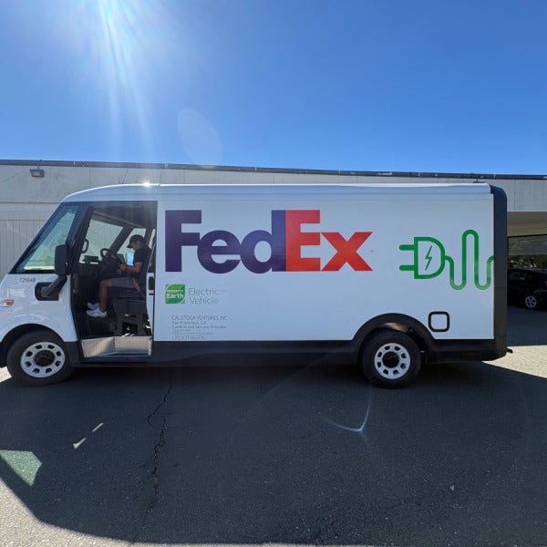 Driver-side view of a FedEx BrightDrop electric delivery van with FedEx and Priority Earth graphics.