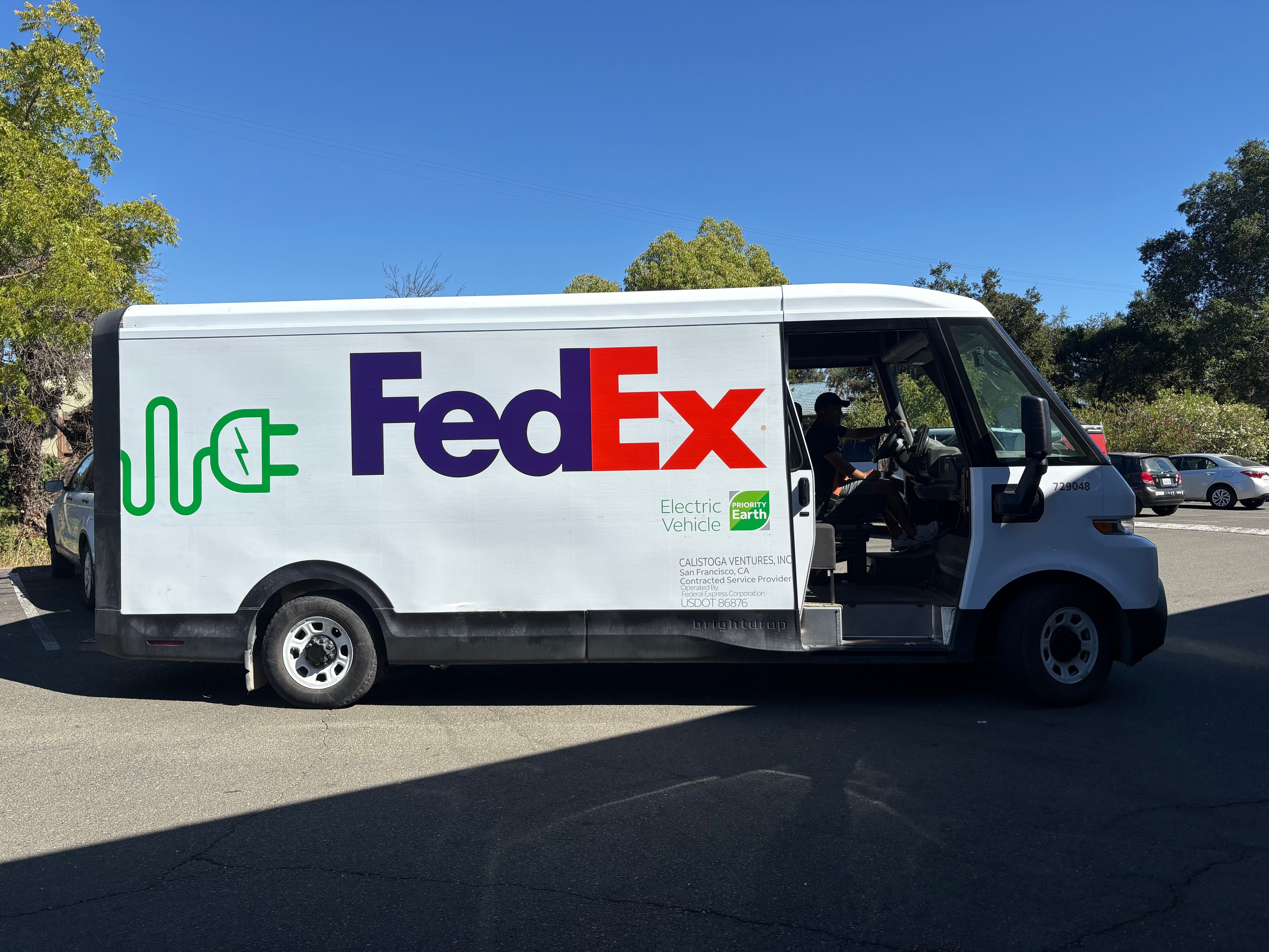 Passenger-side view of a FedEx BrightDrop electric delivery van with FedEx and electric vehicle graphics.