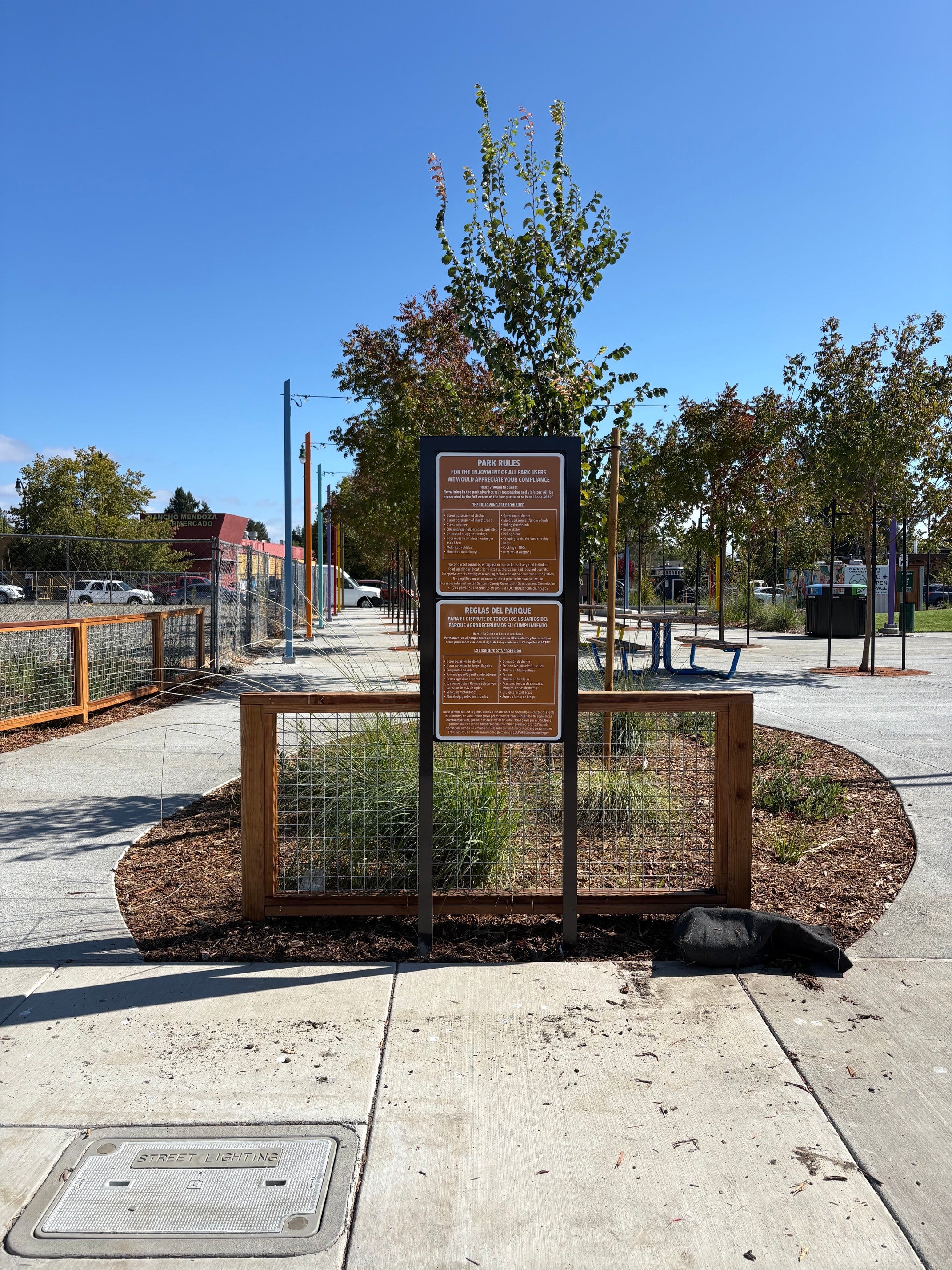 Bilingual Plaza Permanente park rules sign beside a walkway