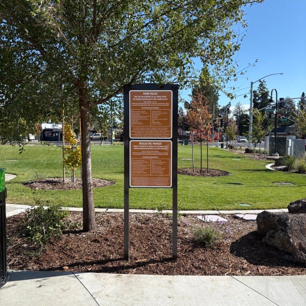 Freestanding bilingual park rules sign in a landscaped area at Plaza Permanente in Santa Rosa