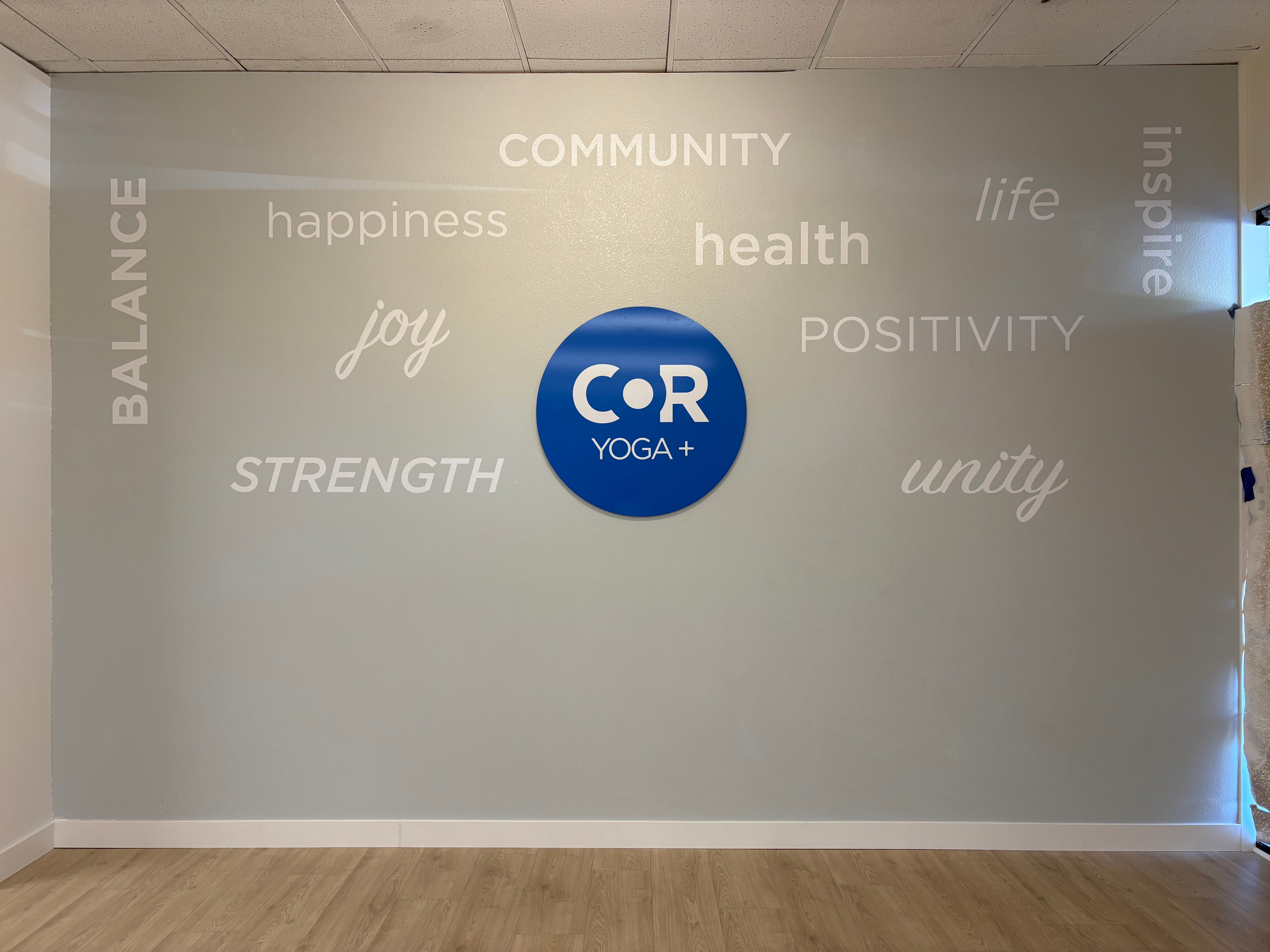 Blue circular COR Yoga+ logo surrounded by white vinyl words on a gray studio wall in Santa Rosa
