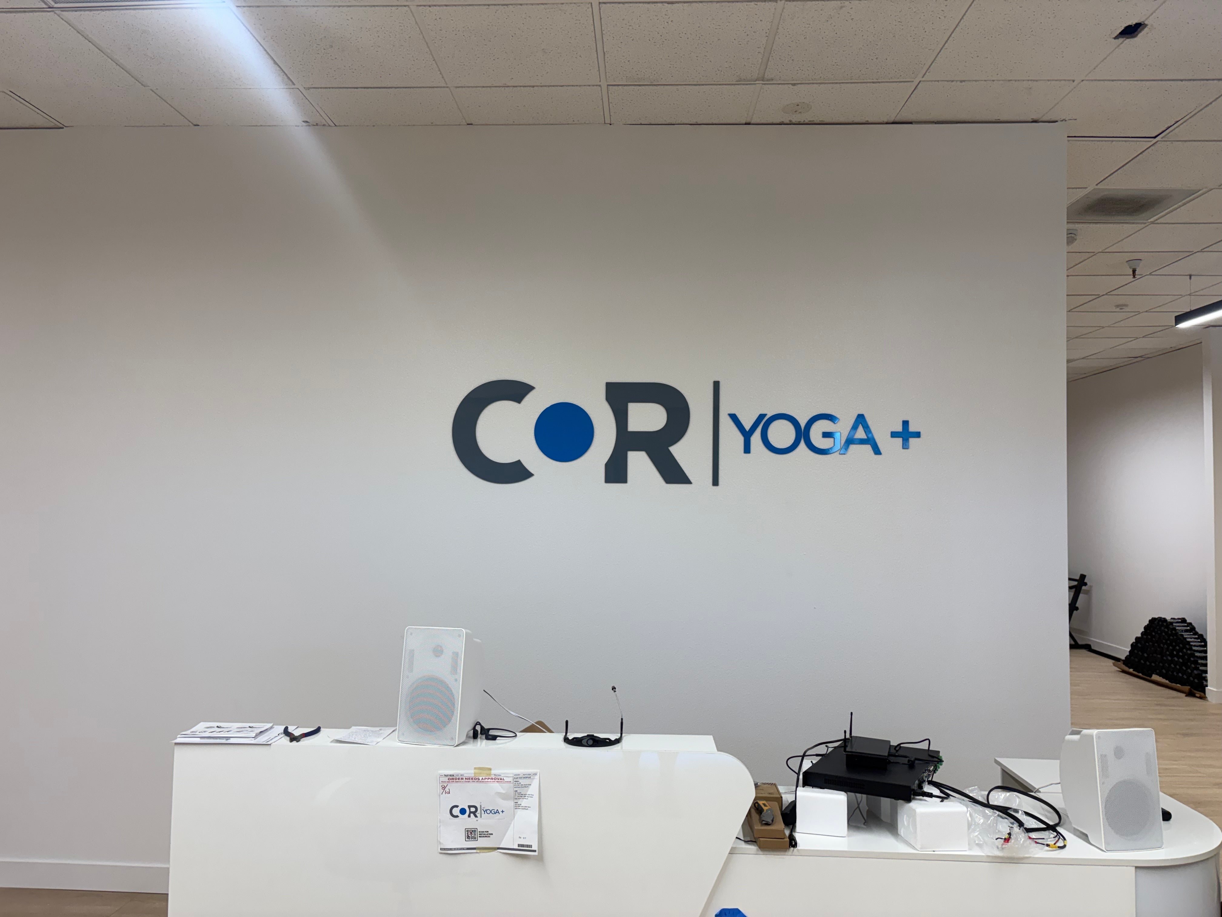 Blue and dark gray COR Yoga+ acrylic logo on the wall behind the studio reception desk