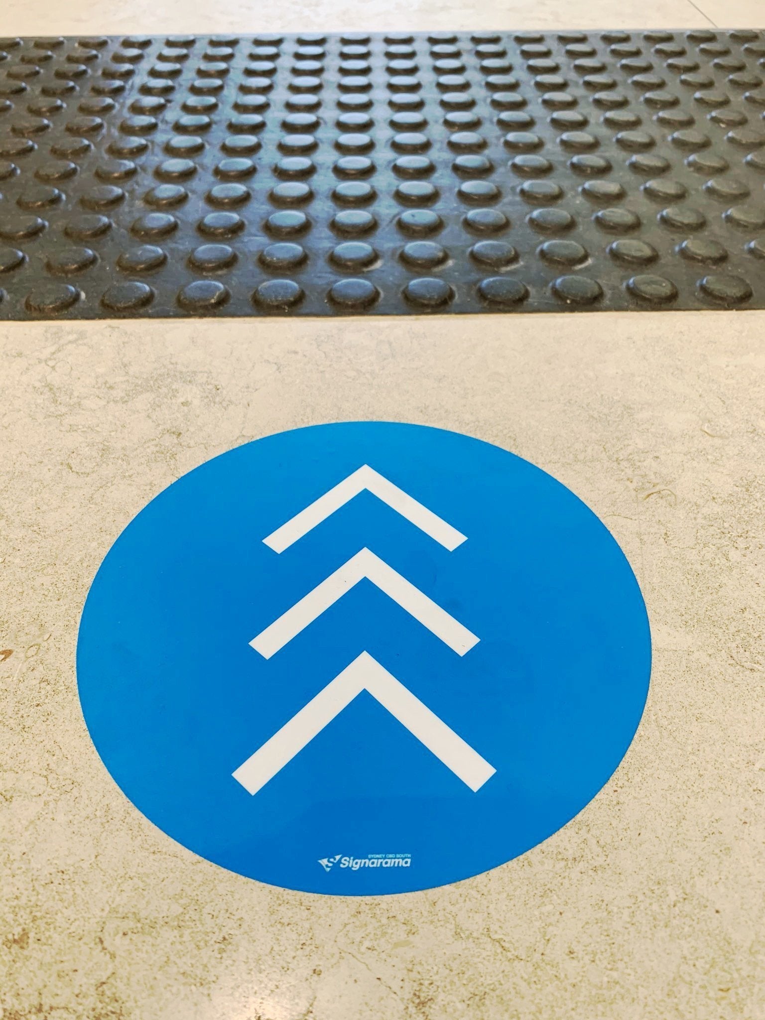 A blue circular vinyl floor decal with arrows for wayfinding