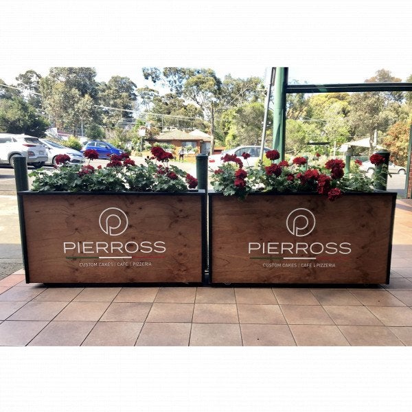 Thick timber cafe barriers with flowers planted in the top and with white branded elements on the timber