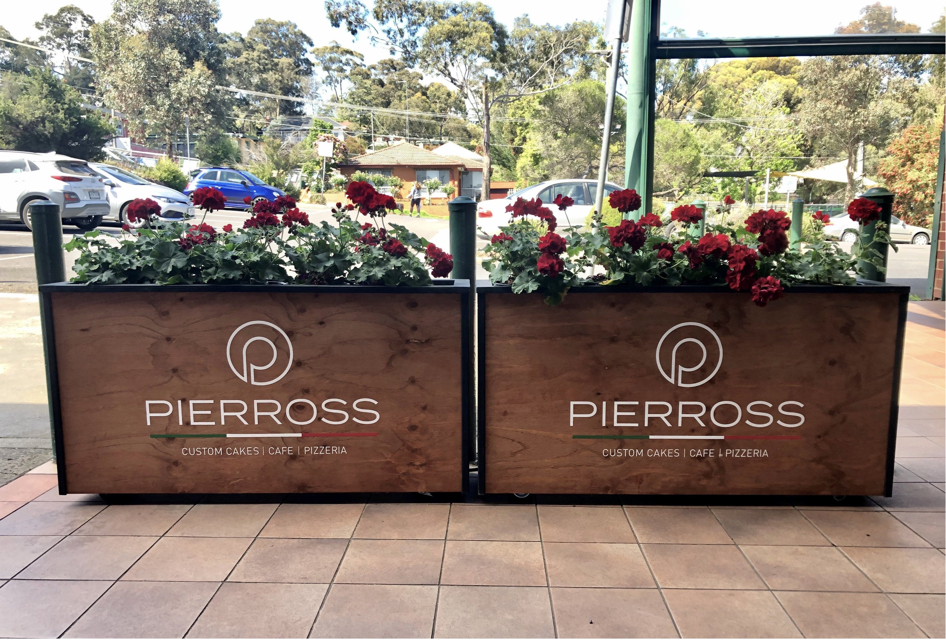 Thick timber cafe barriers with flowers planted in the top and with white branded elements on the timber