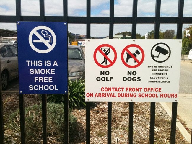 Safety Sign attached to a school fence. The sign warns about smoking, golf, dogs and surveillance