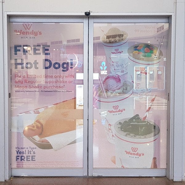 One Way Vision Window on the glass entrance doors of a shopping centre. The graphic is for a cafe and a new free hot dog promotion.