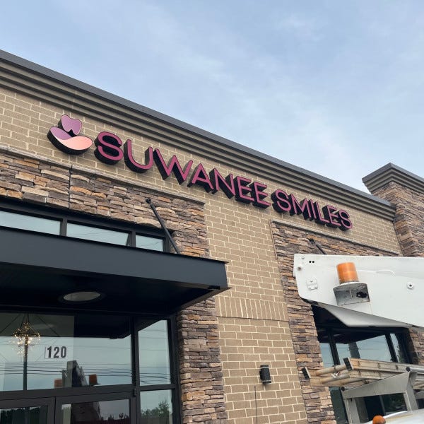 Custom pink and white illuminated channel letter building sign with tooth logo for Suwanee Smiles, installed by Signarama Roswell